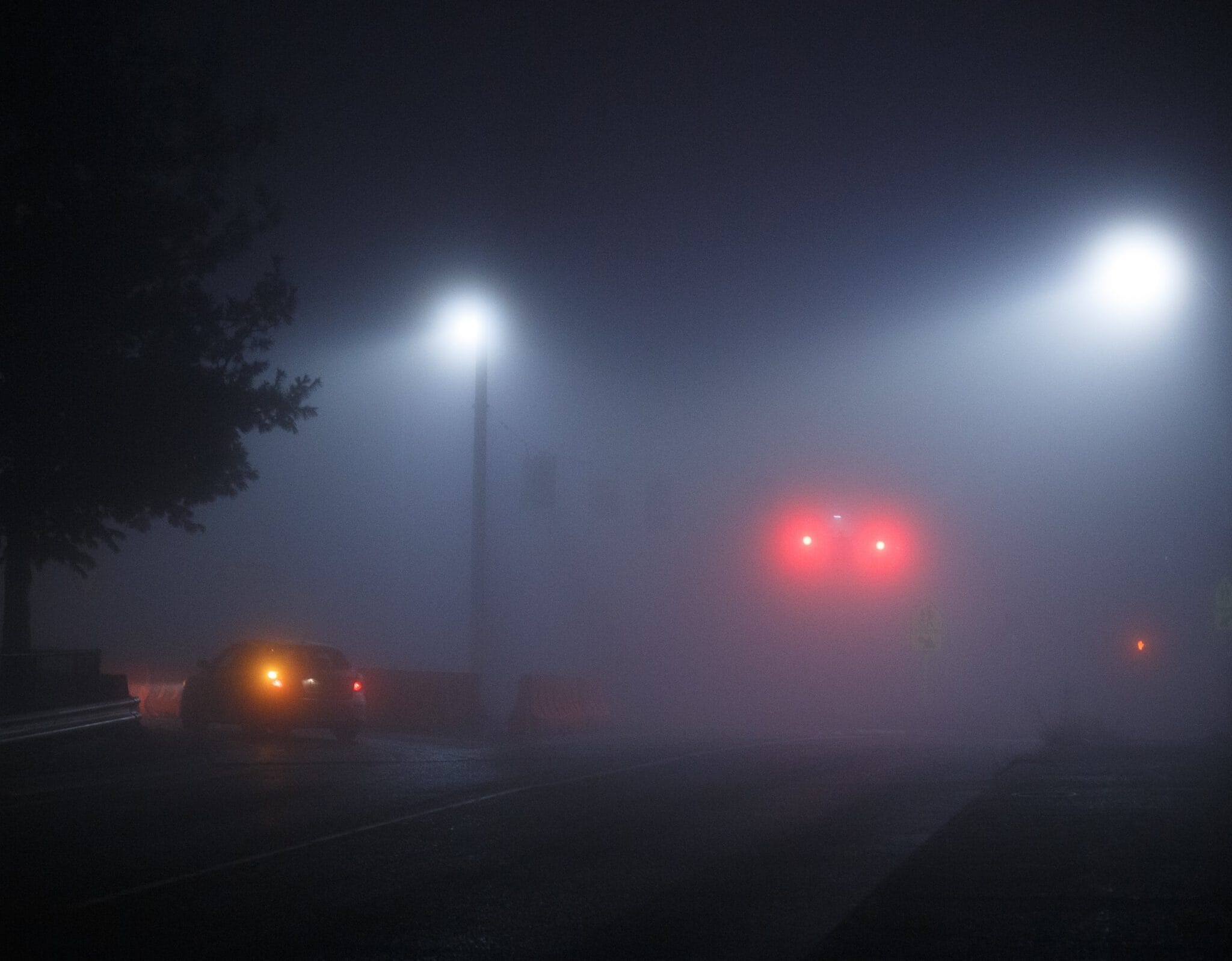 A foggy night with street lights and ambiguous car tail lights vaguely showing through the mist. Several nondescript sillohuettes are visible in front of the light.